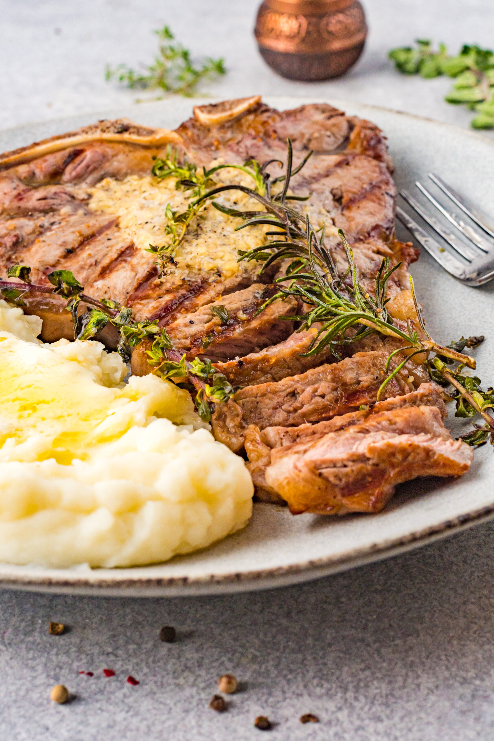 Front view of T Bone Steak on a white plate served with mashed potatoes.