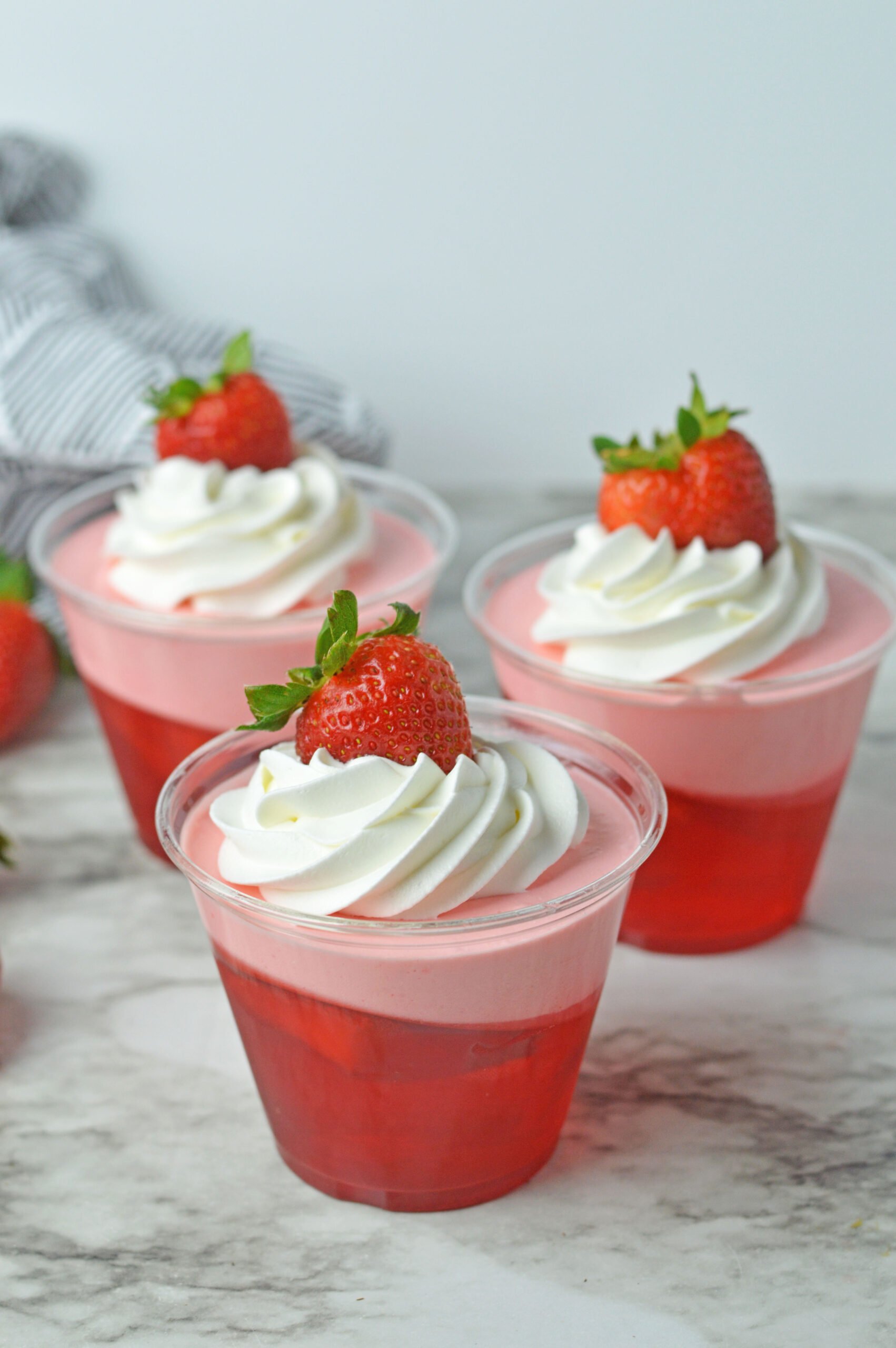 Front view of Strawberry Jello Parfait in plastic cups topped with whipped cream and a strawberry.