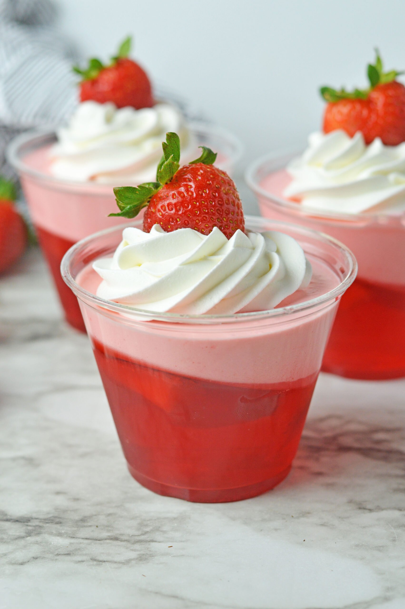 Front view of Strawberry Jello Parfait in plastic cups topped with whipped cream and a strawberry.