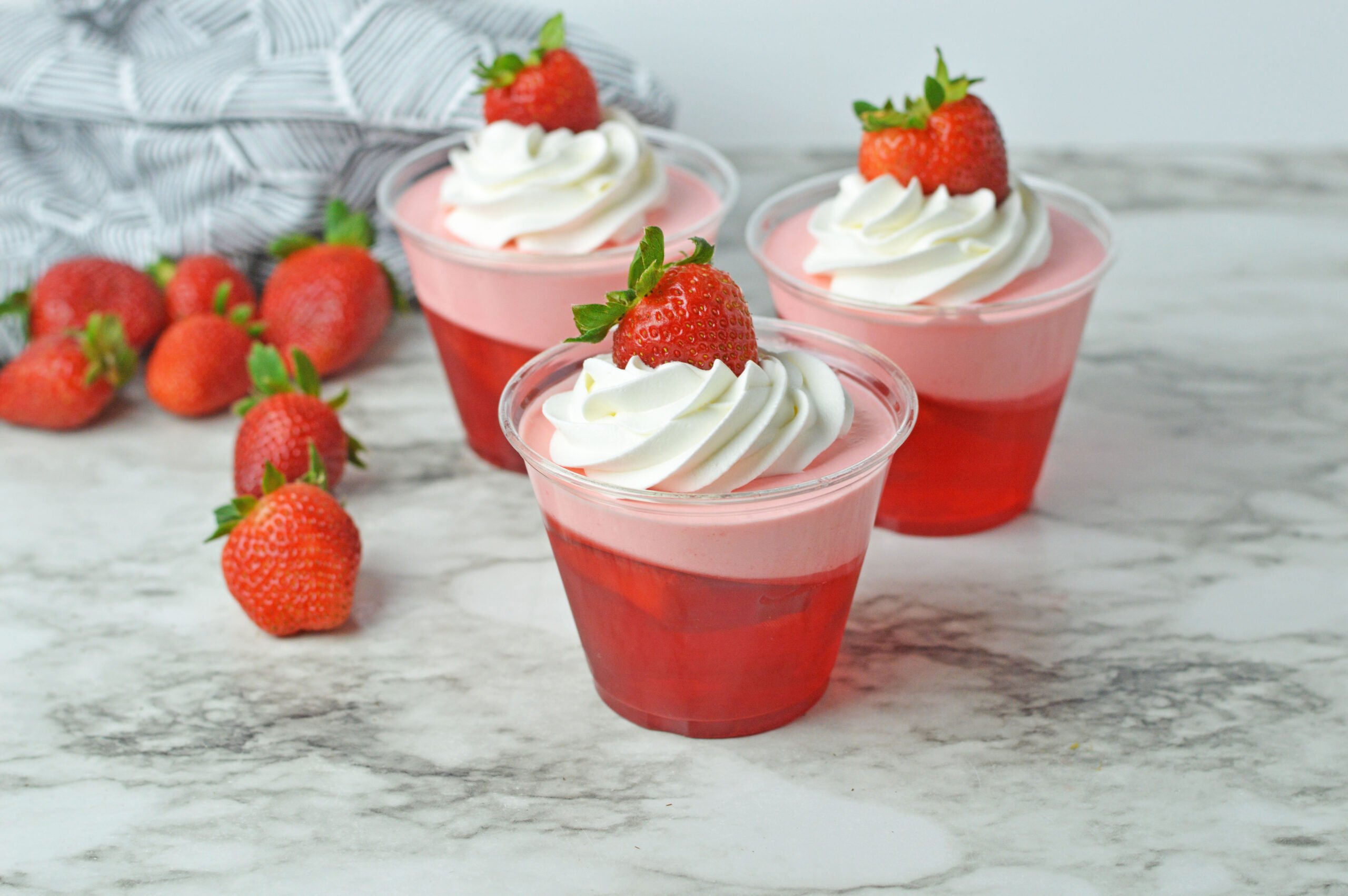 Front view of Strawberry Jello Parfait in plastic cups topped with whipped cream and a strawberry.