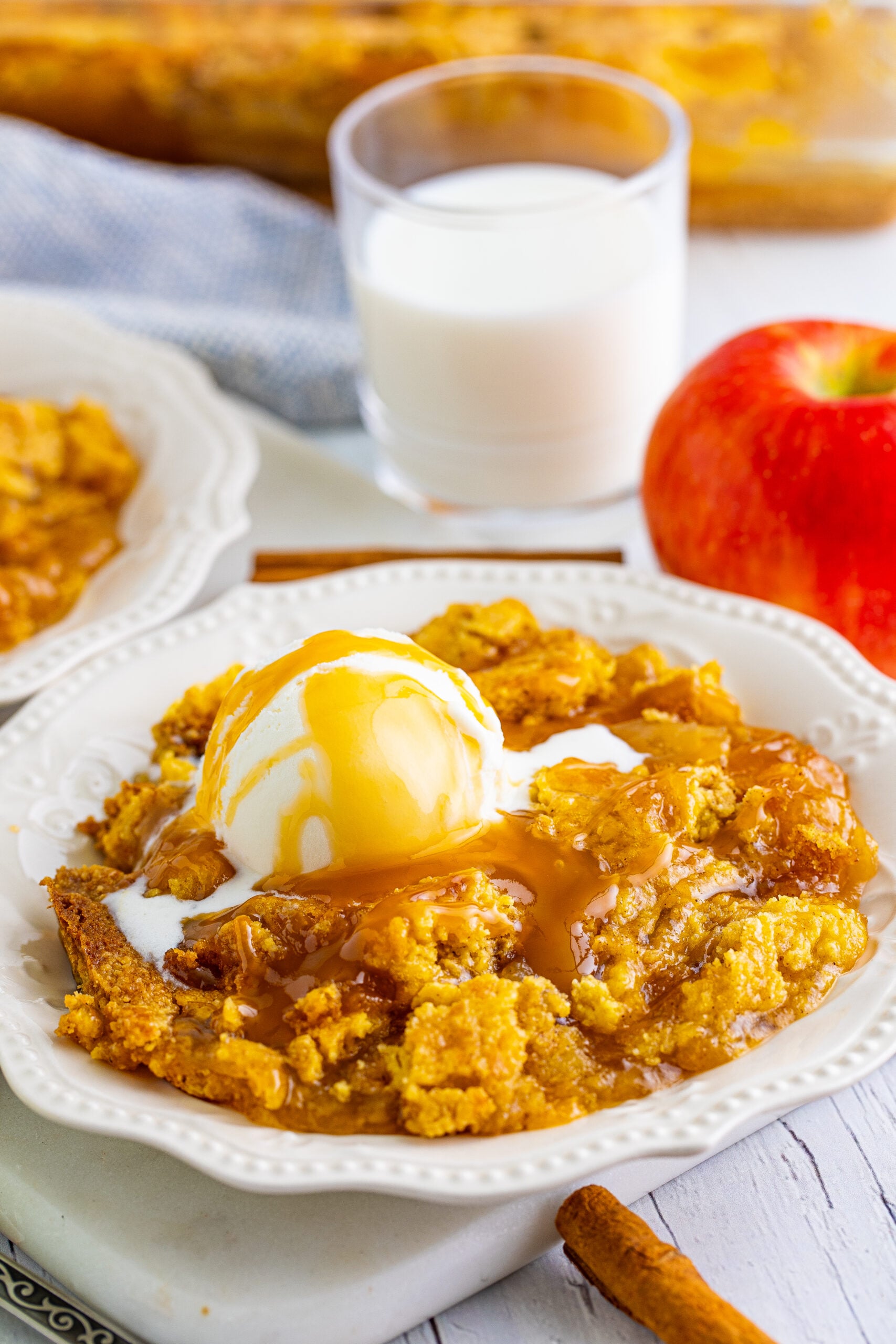 Close up shot of caramel apple dump cake topped with vanilla ice cream and caramel sauce.