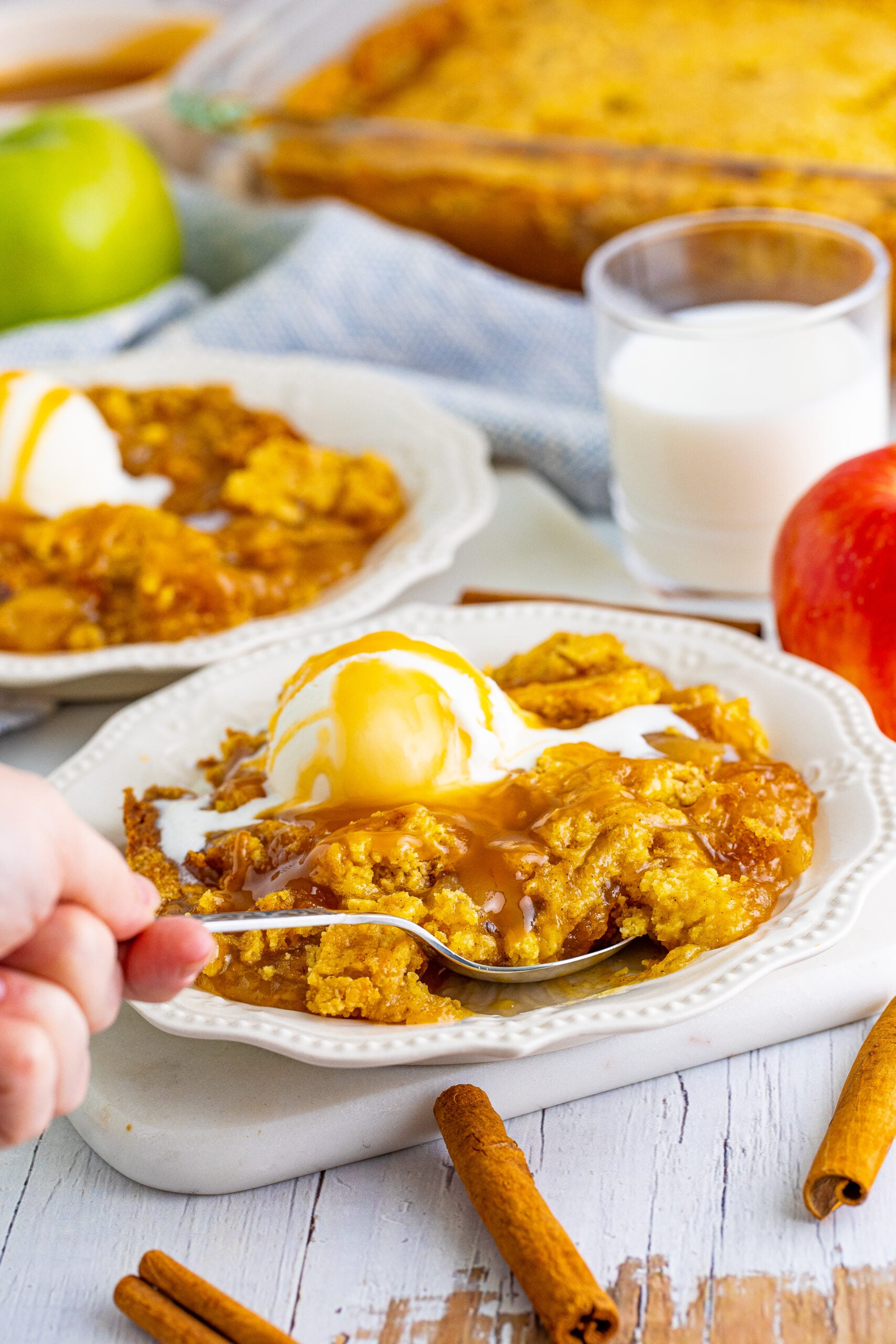 Close up shot of a spoon removing a bite of caramel apple dump cake from a white plate.