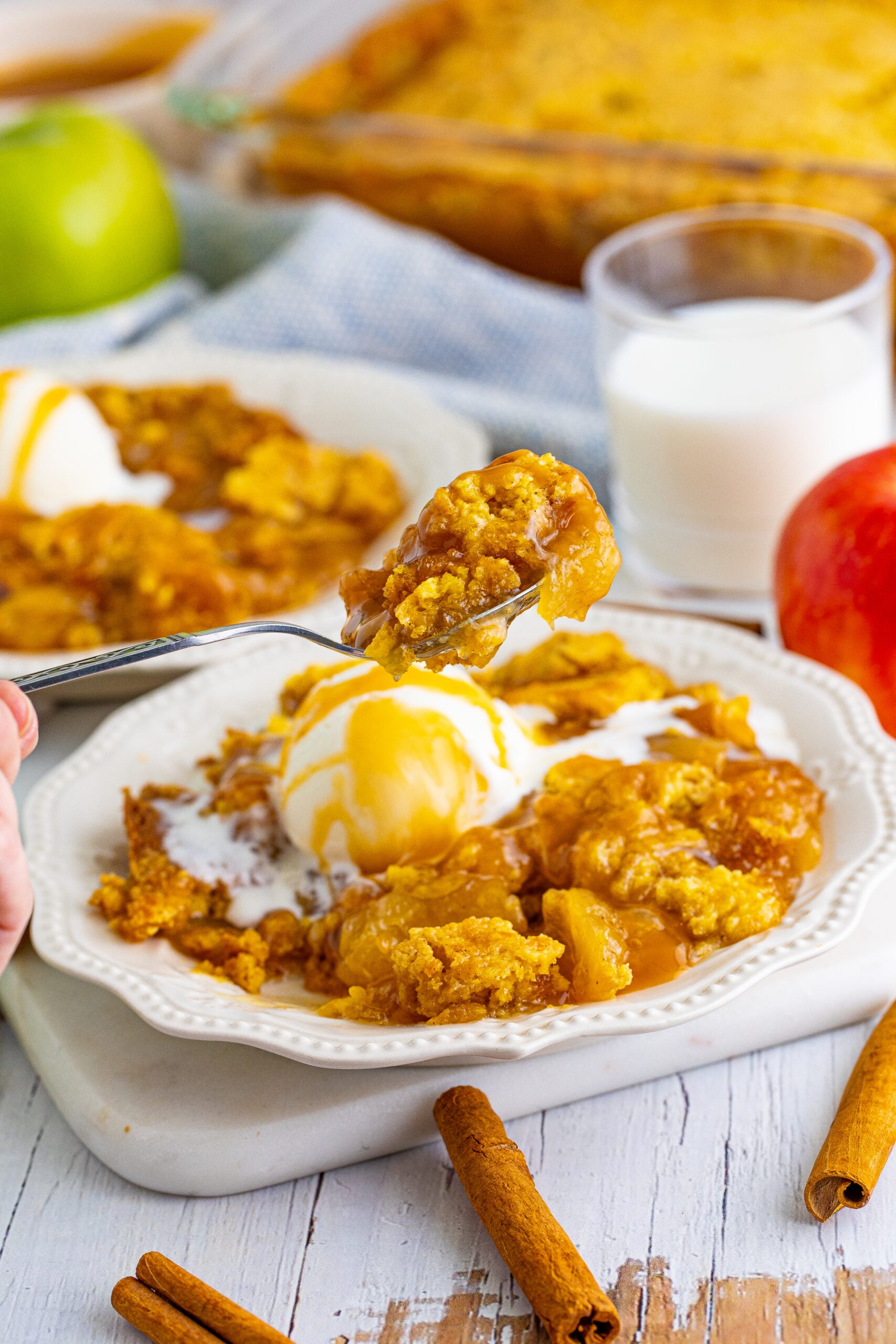 Close up shot of a spoon removing a bite of caramel apple dump cake from a white plate.