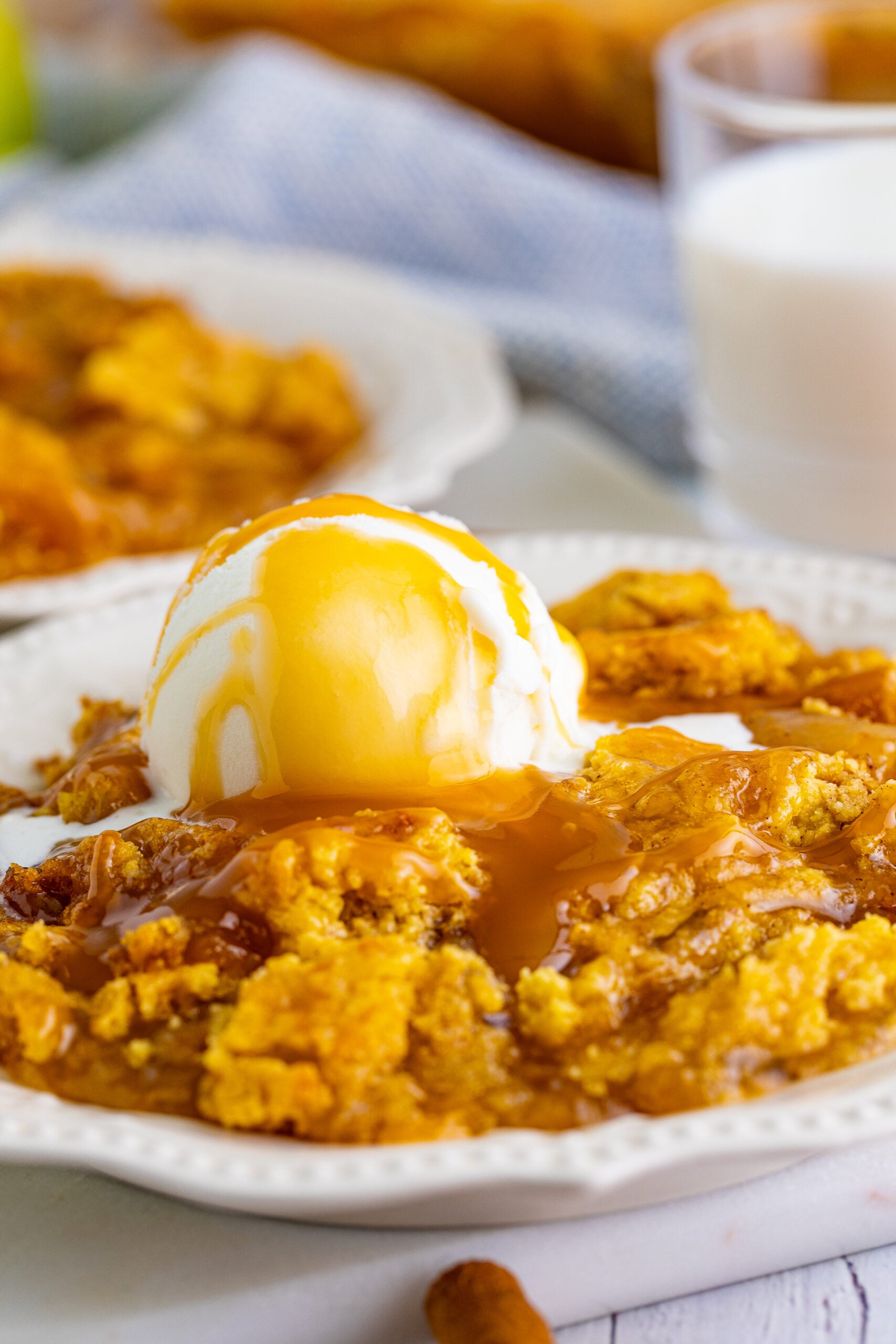 Close up shot of caramel apple dump cake topped with vanilla ice cream and caramel sauce.
