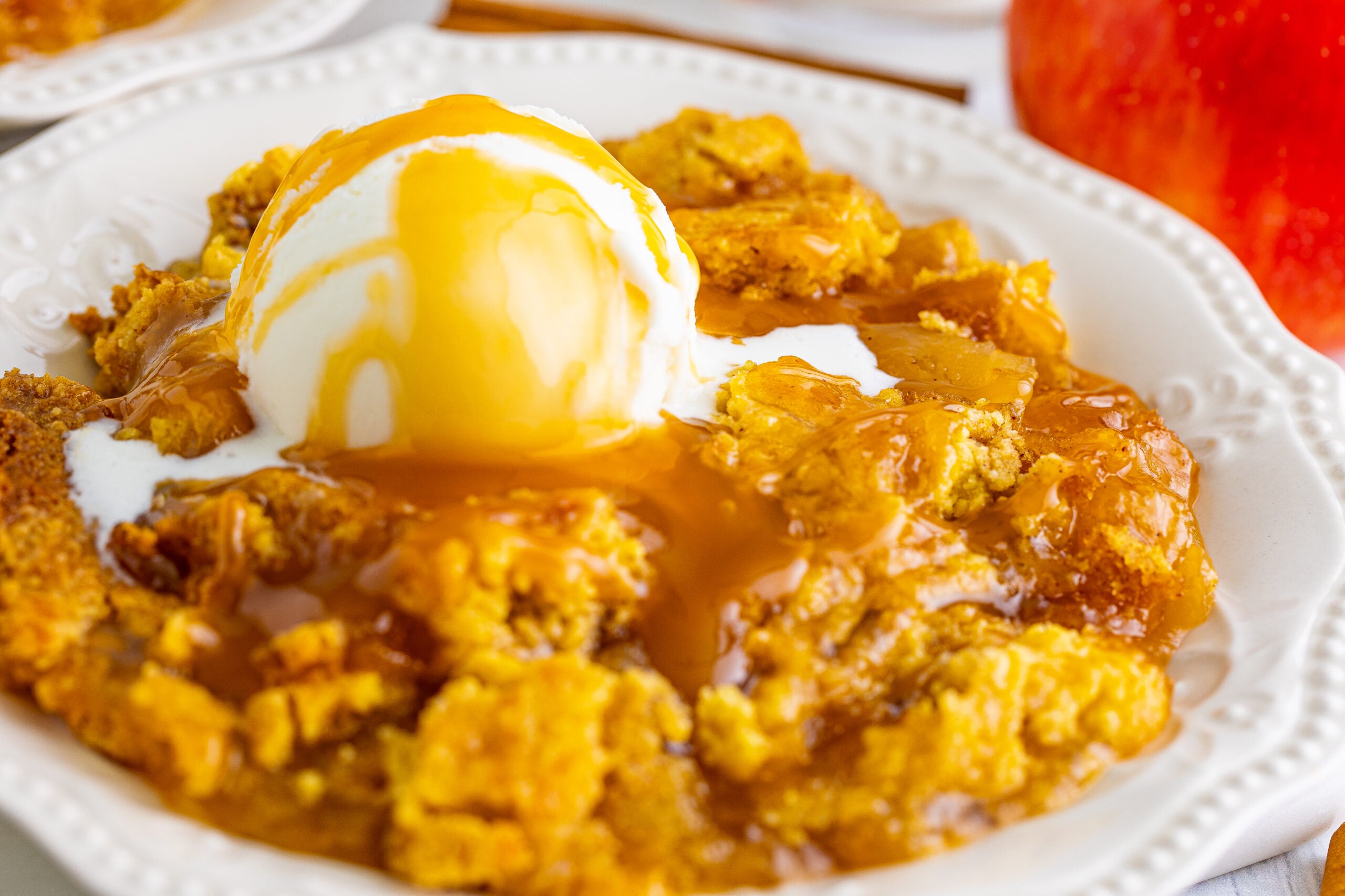 Close up shot of caramel apple dump cake topped with vanilla ice cream and caramel sauce.