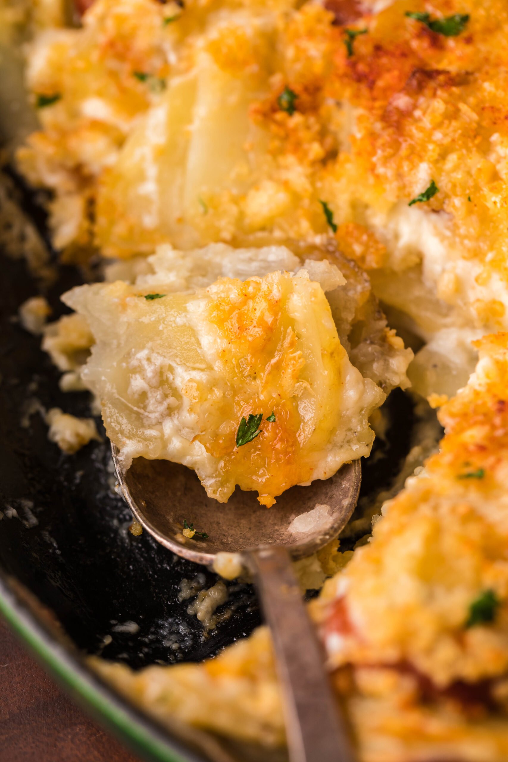 Au Gratin Potatoes & Sausage in a cast iron skillet with a spoon scooping some