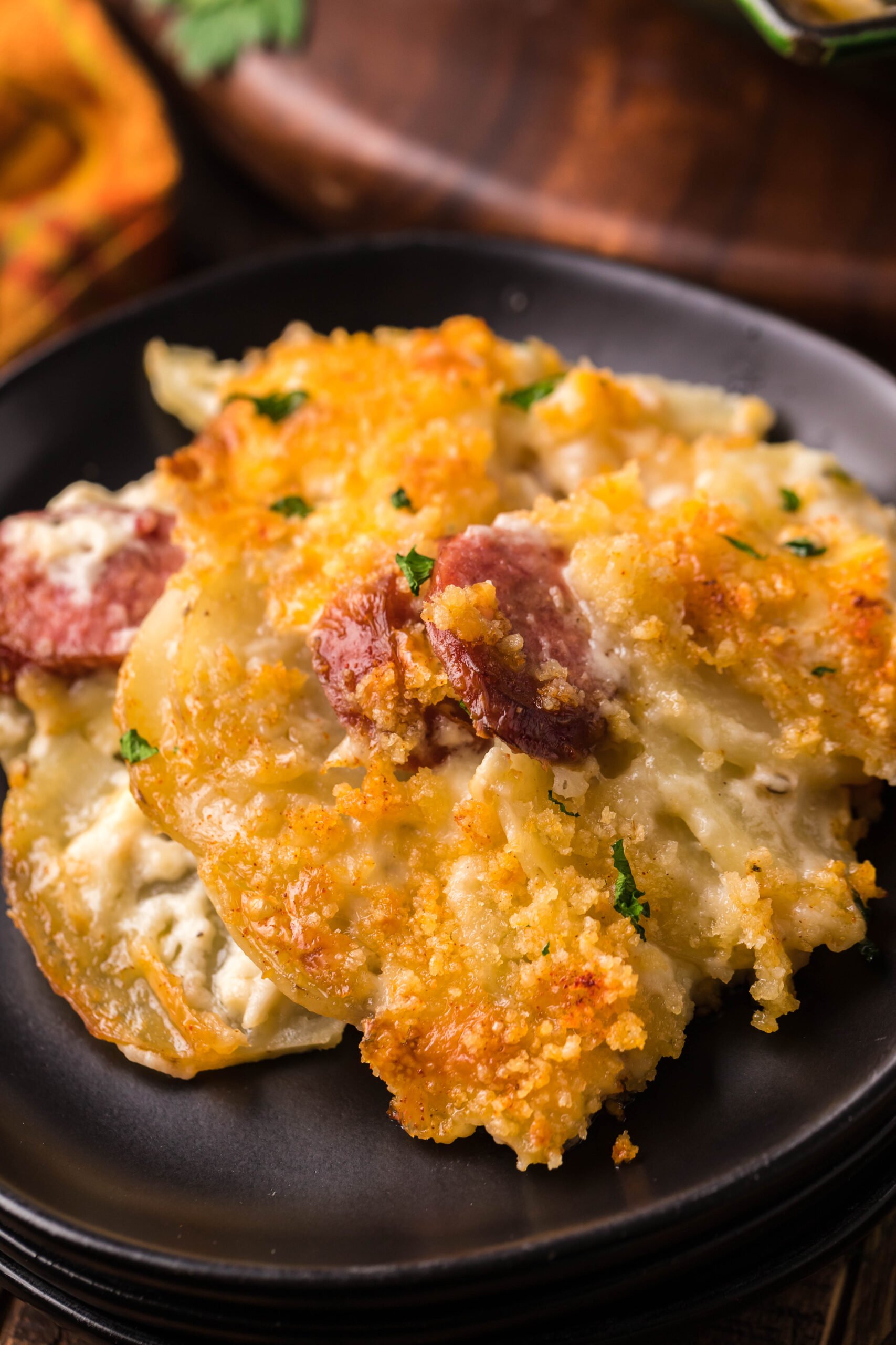 Close up view of a serving of Au Gratin Potatoes & Ham on a black plate.