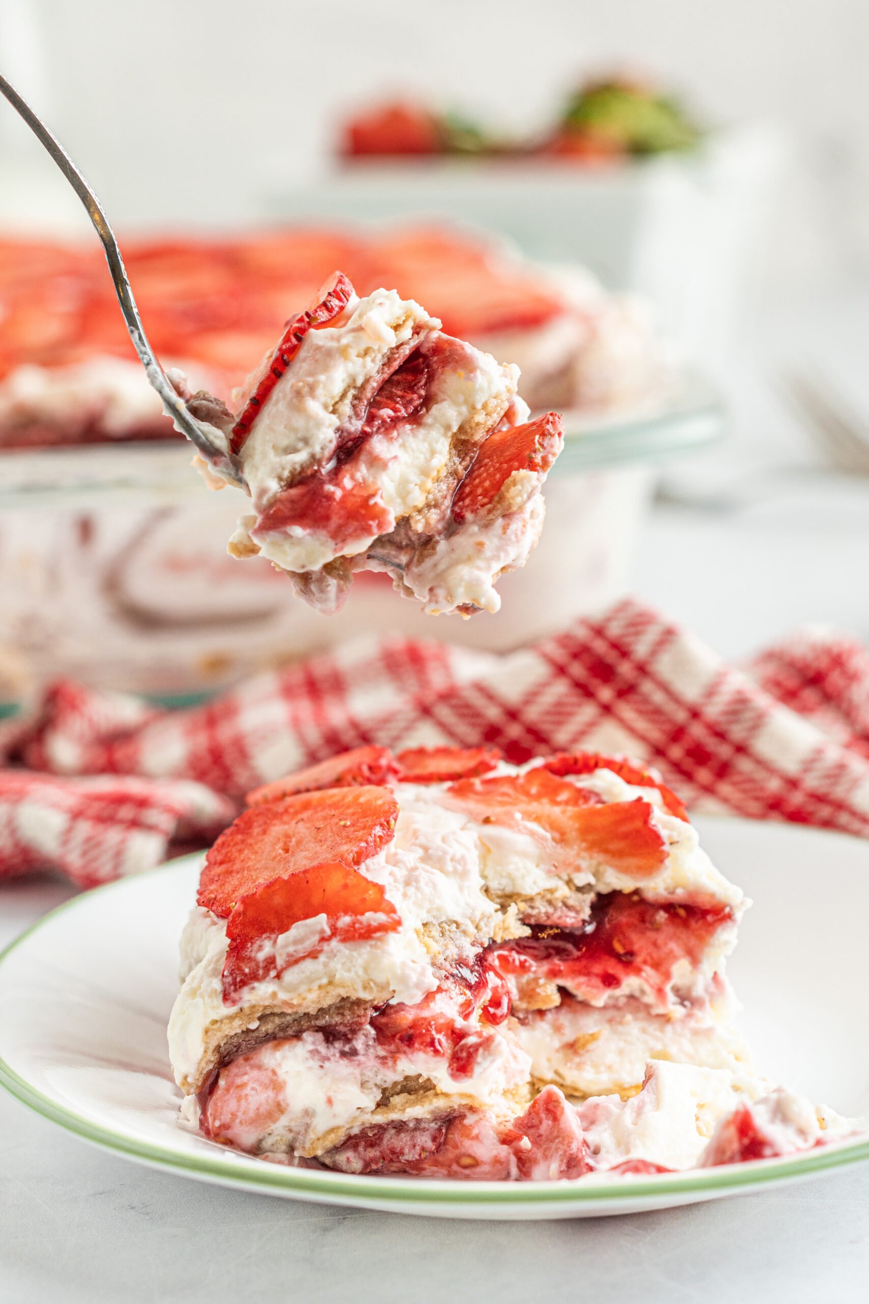 A piece of Strawberry Icebox Cake on a white and green plate with a bite being removed with a silver fork. 