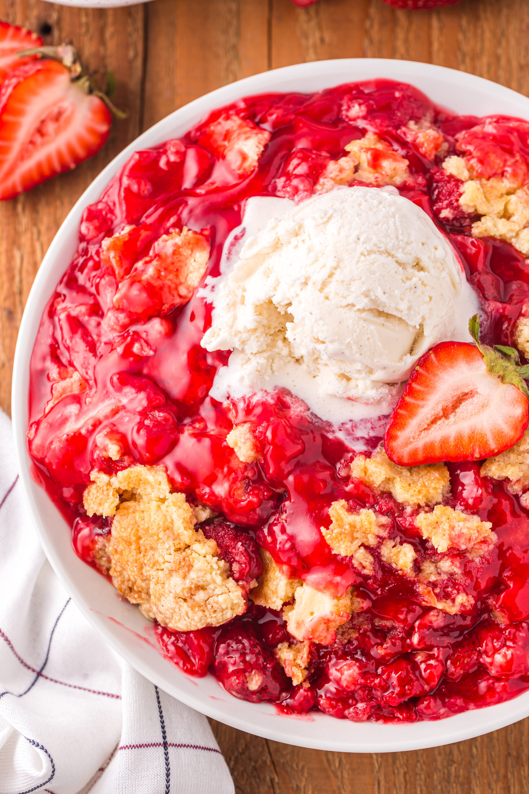 overhead view of a serving of Strawberry Dump Cake in a white bowl topped with a scoop of ice cream.
