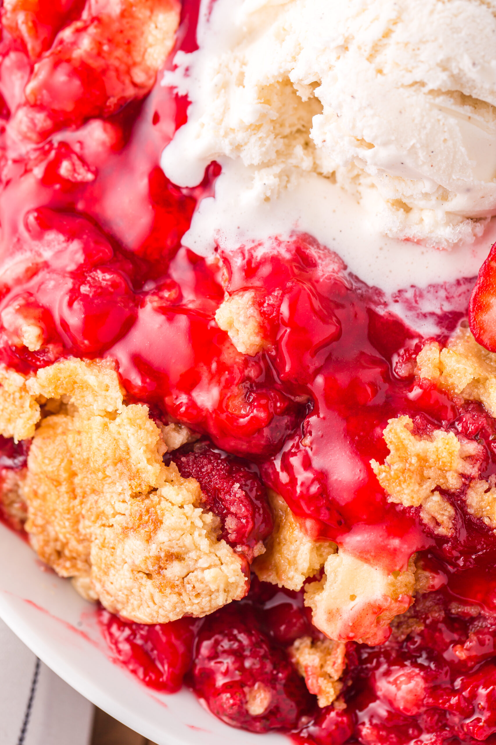 Close up view of a serving of Strawberry Dump Cake in a white bowl topped with a scoop of ice cream.