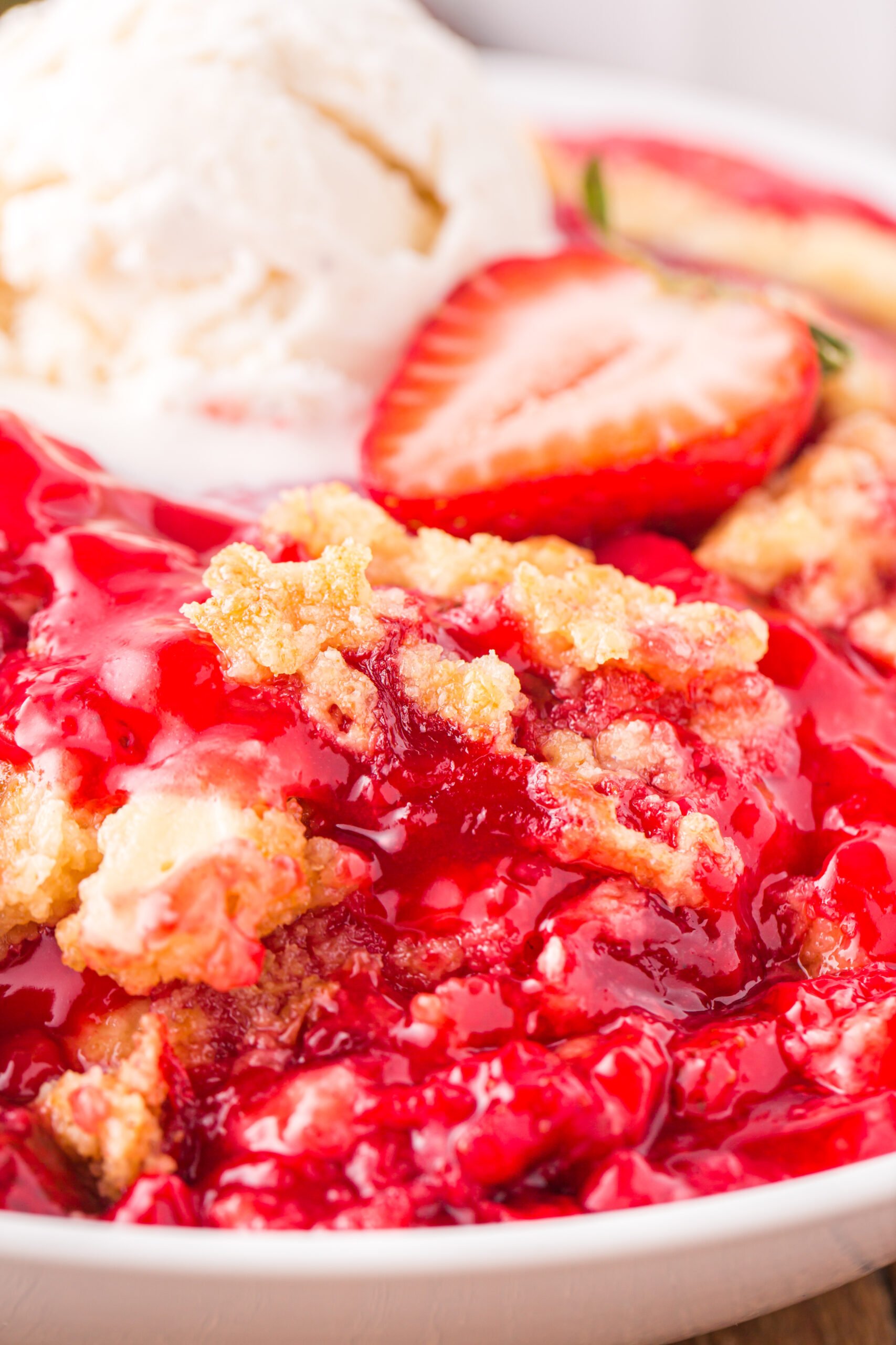 Close up view of a serving of Strawberry Dump Cake in a white bowl topped with a scoop of ice cream.