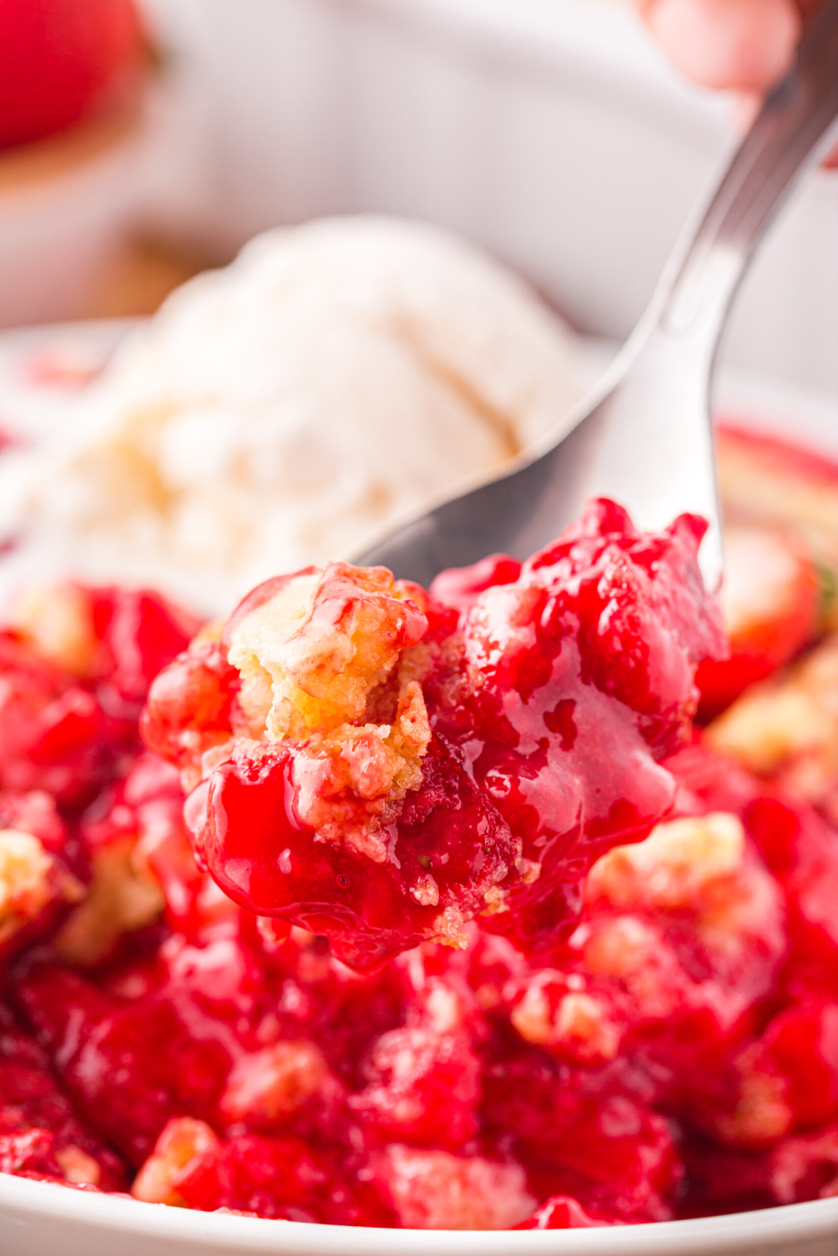 Close up view of a bite of Strawberry Dump Cake on a silver spoon.