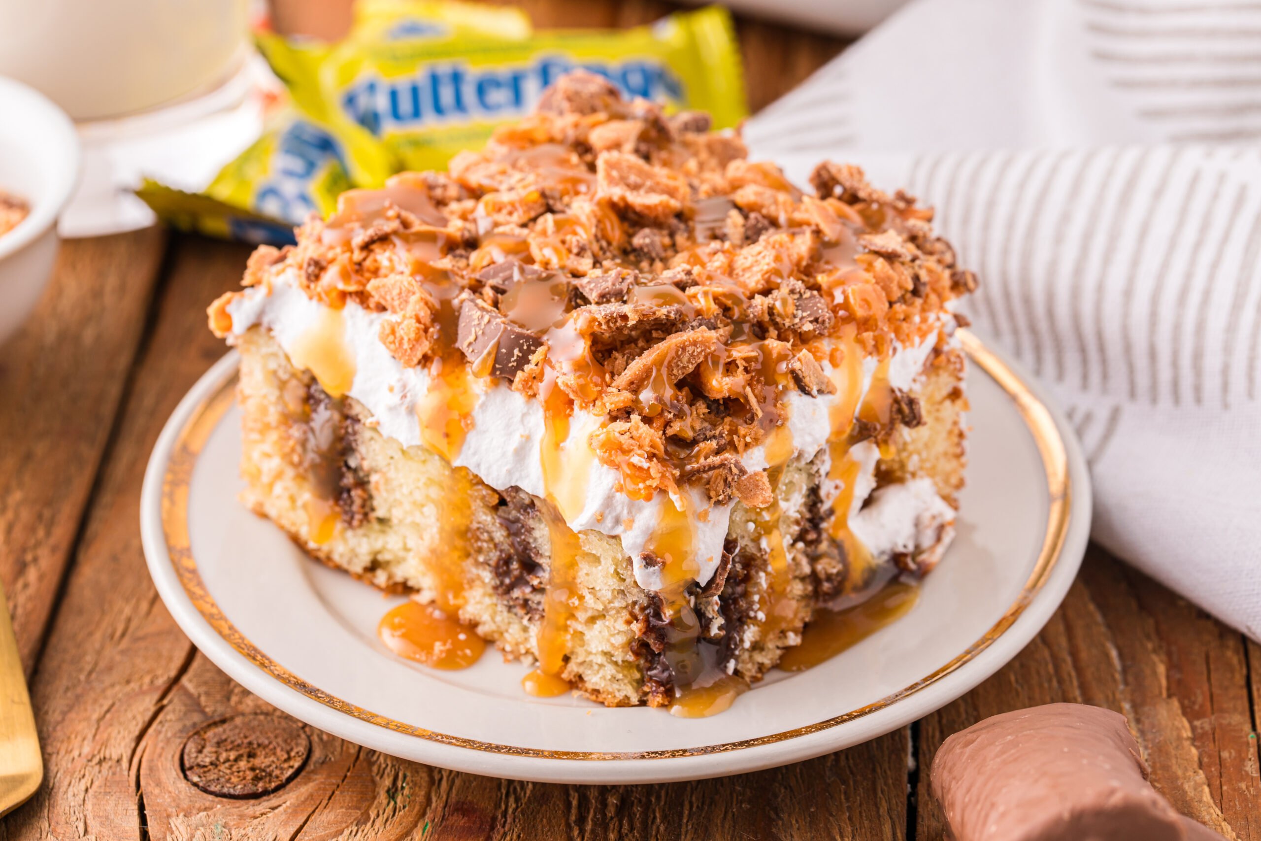 Butterfinger Poke Cake on a white plate sitting on a wooden table 