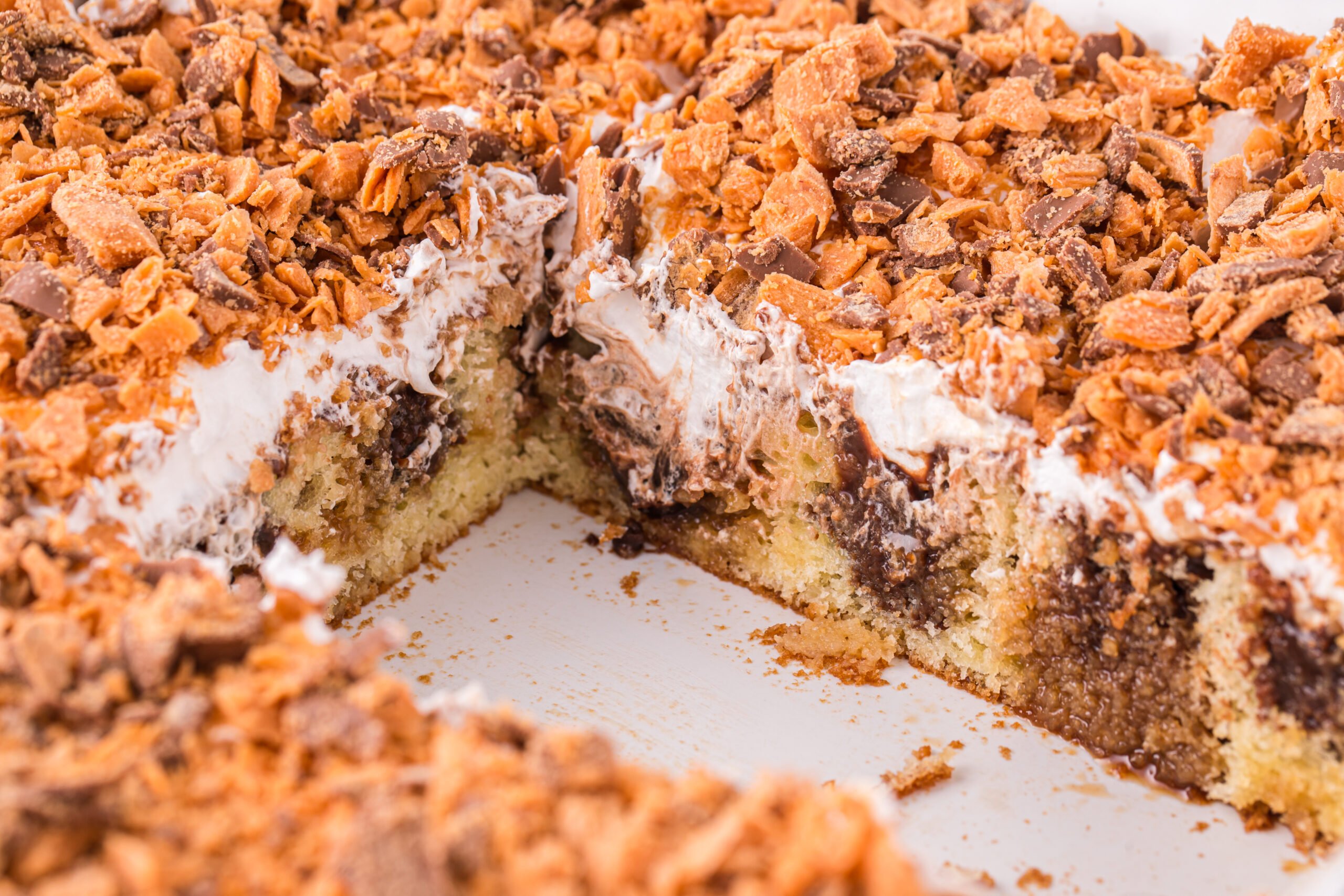 Butterfinger Poke Cake in a white baking dish with a couple slices removed