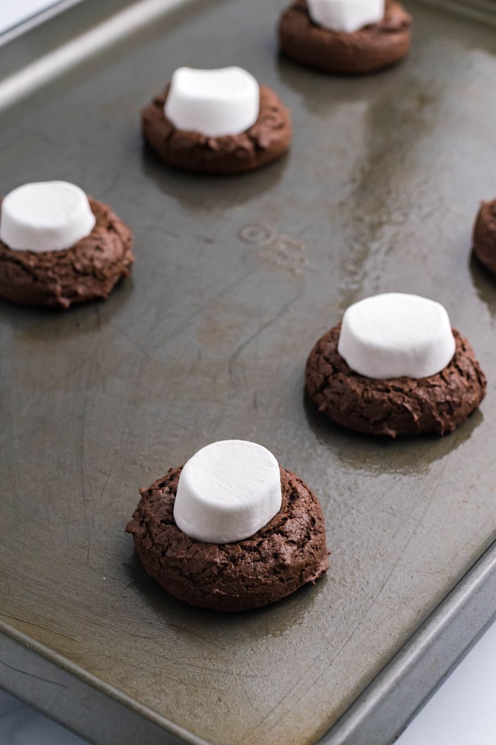 marshmallows sitting on top of chocolate cookie on baking tray 