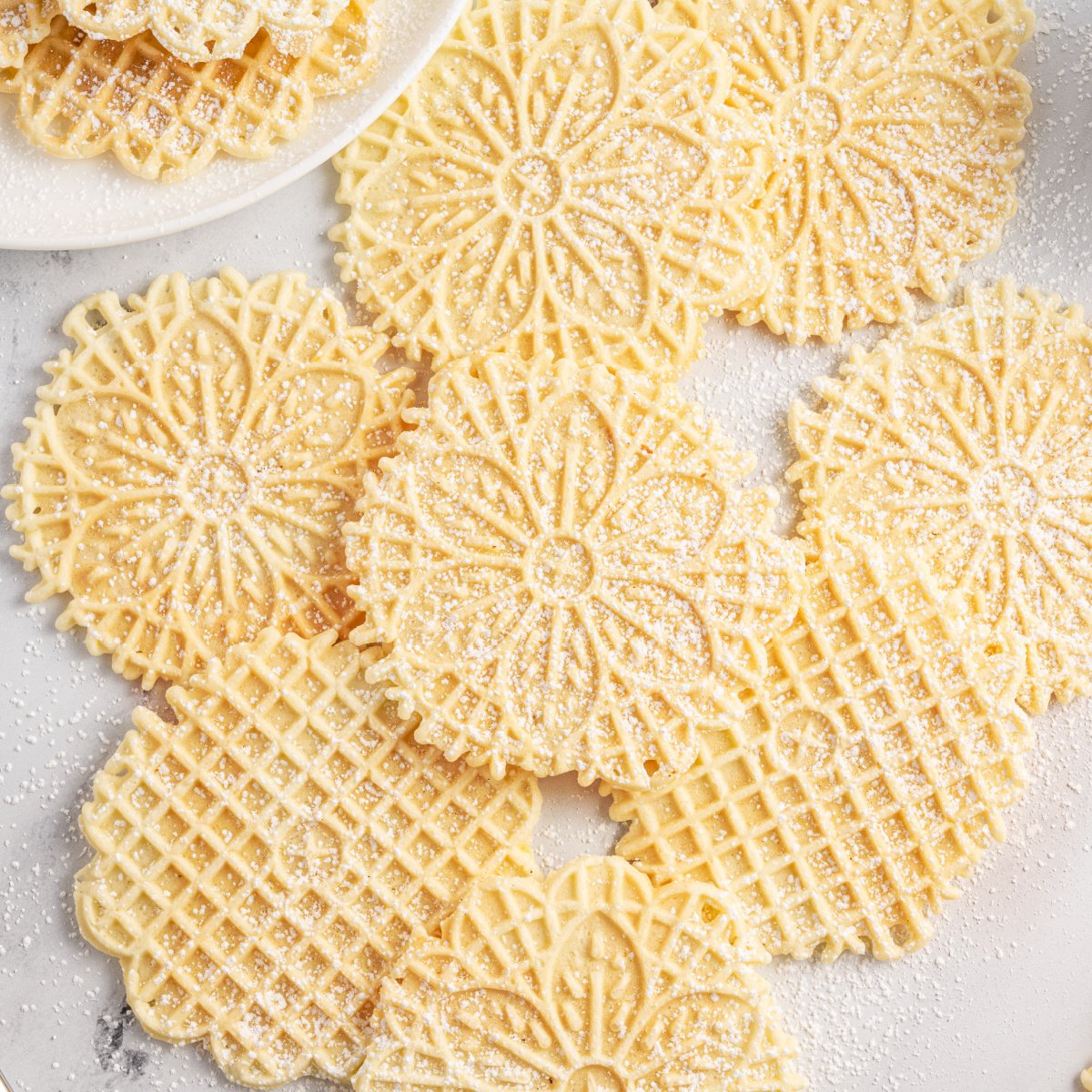 Pizzelles on marble table sprinkled with powdered sugar