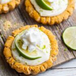 Crumbl Key Lime Pie Cookies on table with lime wedges around and piles of graham cracker crumbs