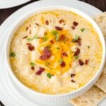 Hash Brown Potato Soup in a white bowl on a plate with saltine crackers on the side