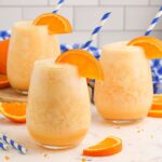 Copycat Orange Julius in three glasses on table with an orange slice on rim and straw in each glass
