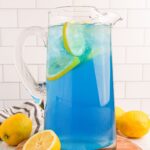 Blue Raspberry Lemonade in a pitcher on table with sliced lemons around it on table
