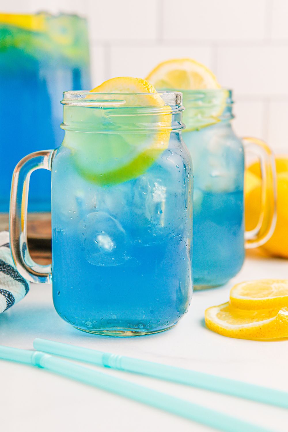 Blue Raspberry Lemonade in mason jars with lemon garnished around them on table 