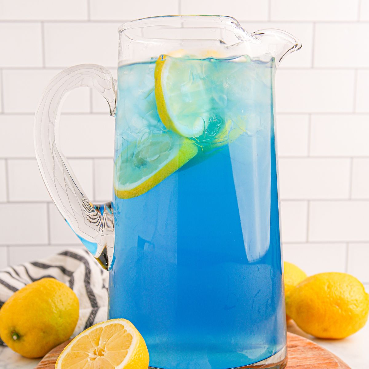 Blue Raspberry Lemonade in a pitcher on table with sliced lemons around it on table