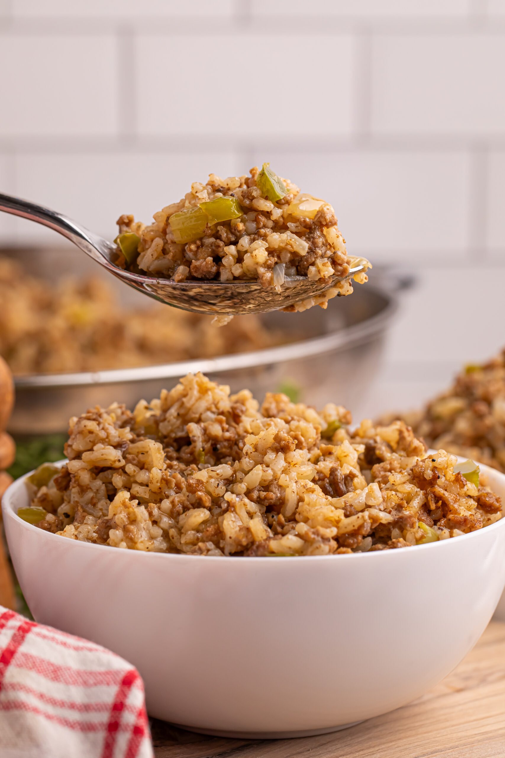 Dirty Rice in a white bowl sitting on a table with a spoon lifting up a bite 