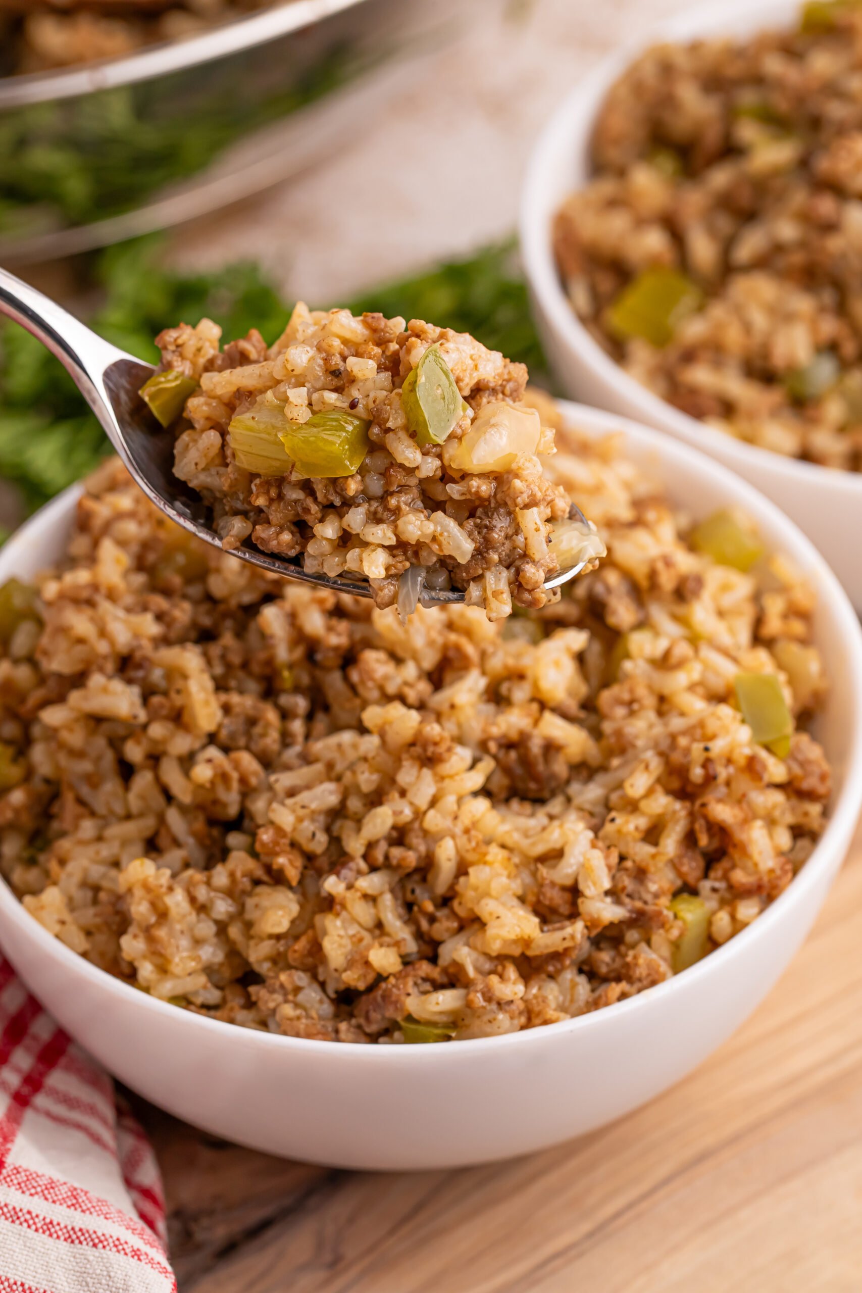 Dirty Rice in a white bowl sitting on a table with a spoon lifting up a bite 