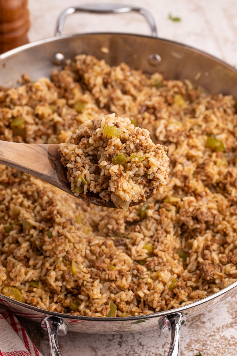 Dirty Rice in a pan with a scoop on a wooden spoon above the pan 
