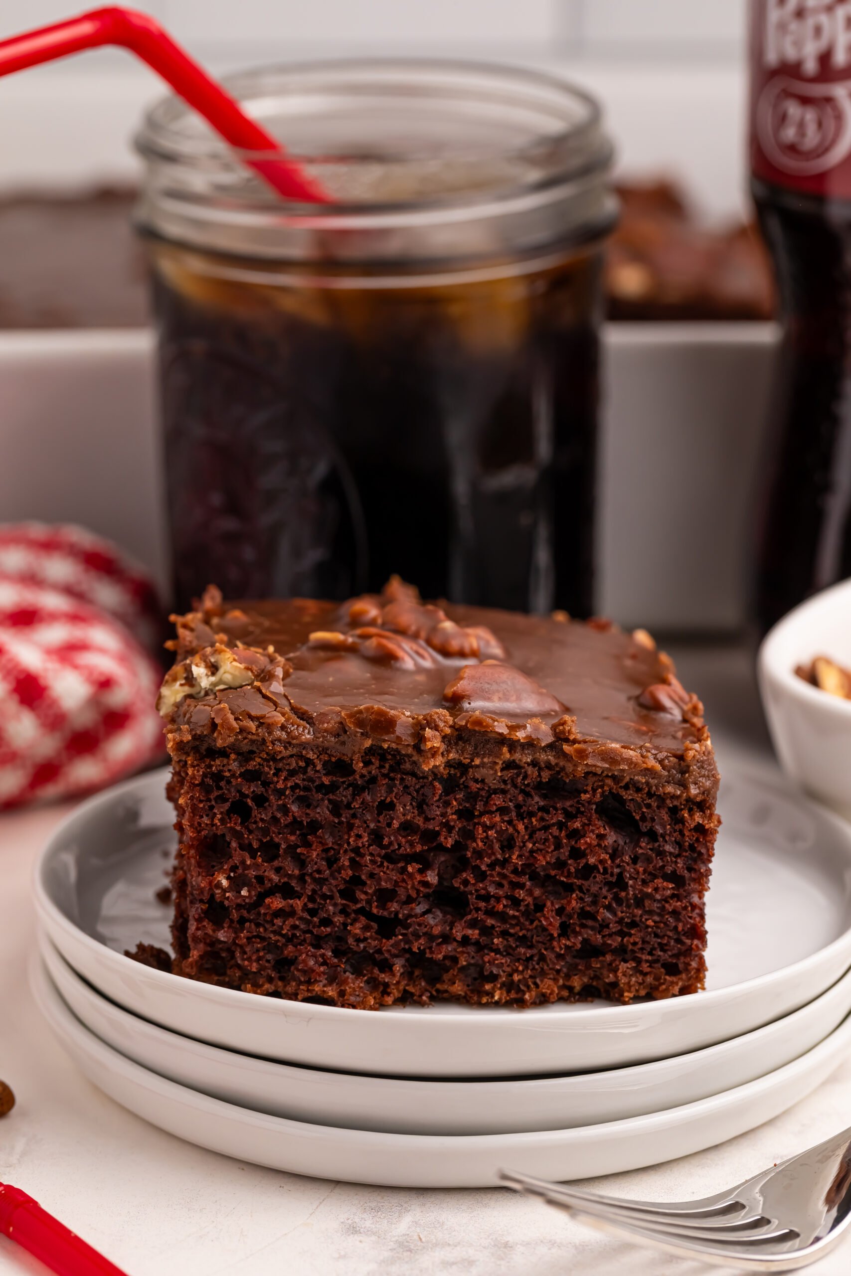 slice of Dr. Pepper Cake on plates with a glass of Dr. Pepper in a glass behind it on the table 