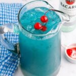 Blue Hawaiian Punch in a pitcher on table with a bowl of cherries on side and a bottle of Barcardi i the background