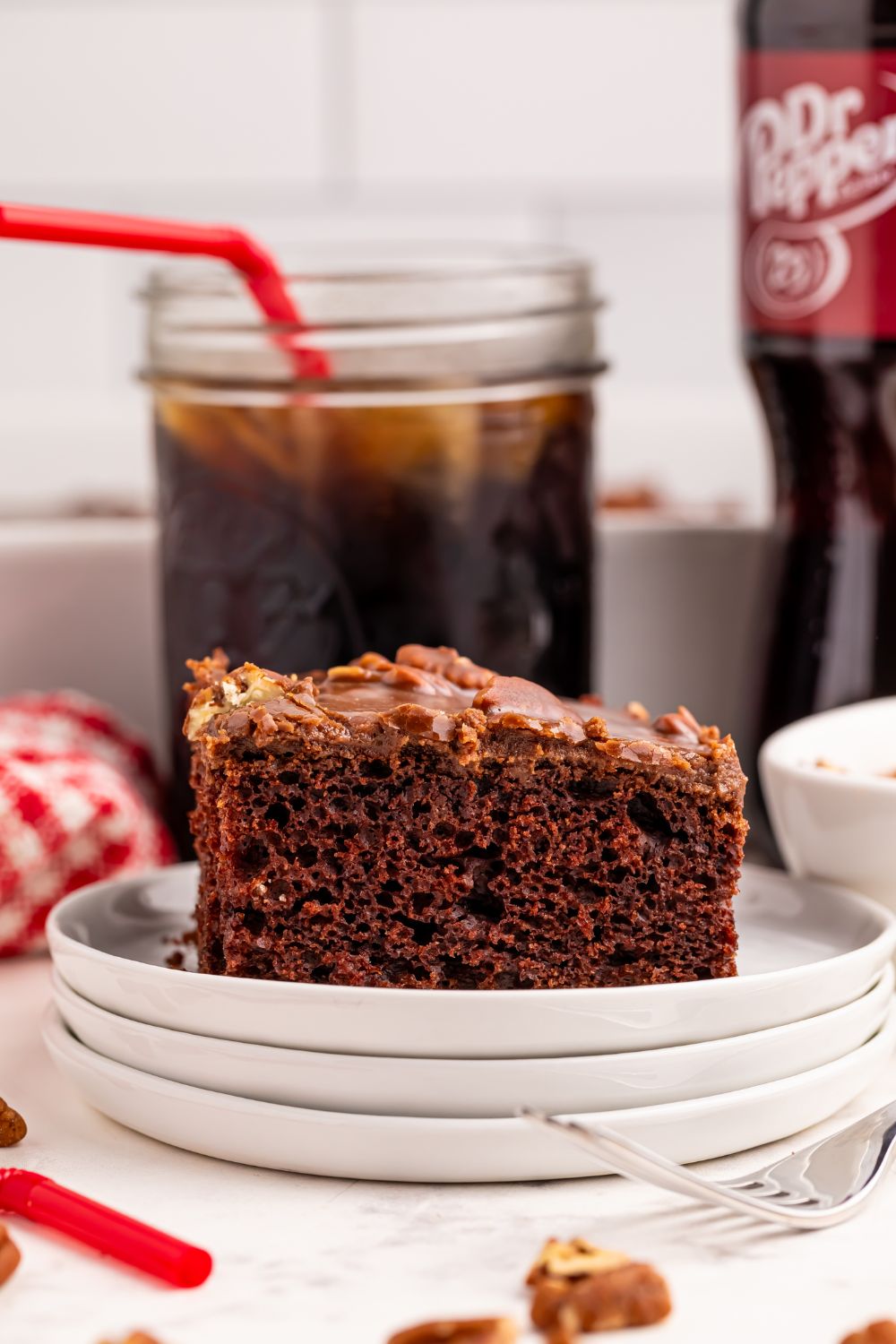 Dr. Pepper Cake sliced on plate with a mason jar of dr pepper sitting behind it on table 