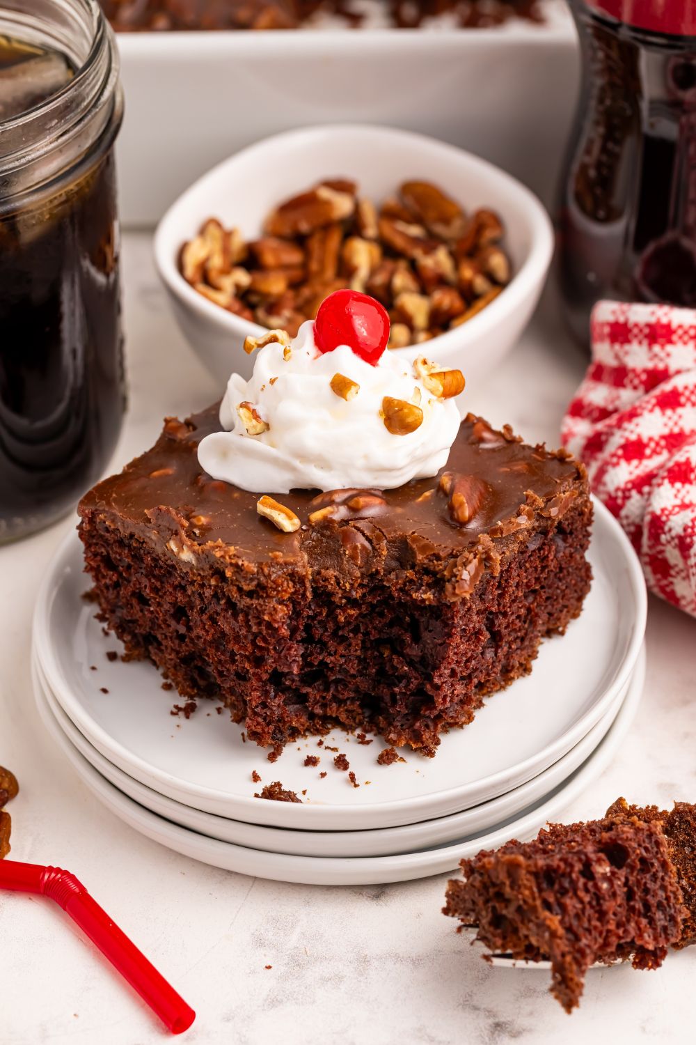 slice of cake on plate with a bite taken out and whippd cream and cherries on top