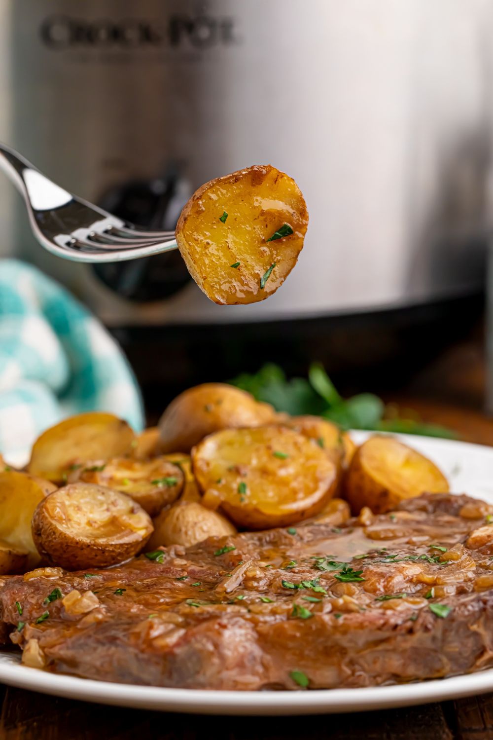 fork with a potato poked on it above plate with steak and potatoes on it