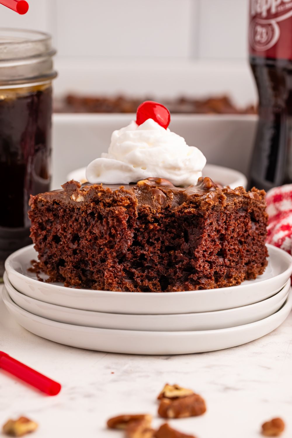 Dr. Pepper Chocolate Cake on a stack of plates topped with whipped cream and a cherry 
