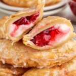 Cherry Cheesecake Hand Pies stacked on table with on cut in half to show the filling