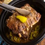 Slow Cooker Mississippi Ribs in crockpot with a rib section being lifted out of crockpot with tongs