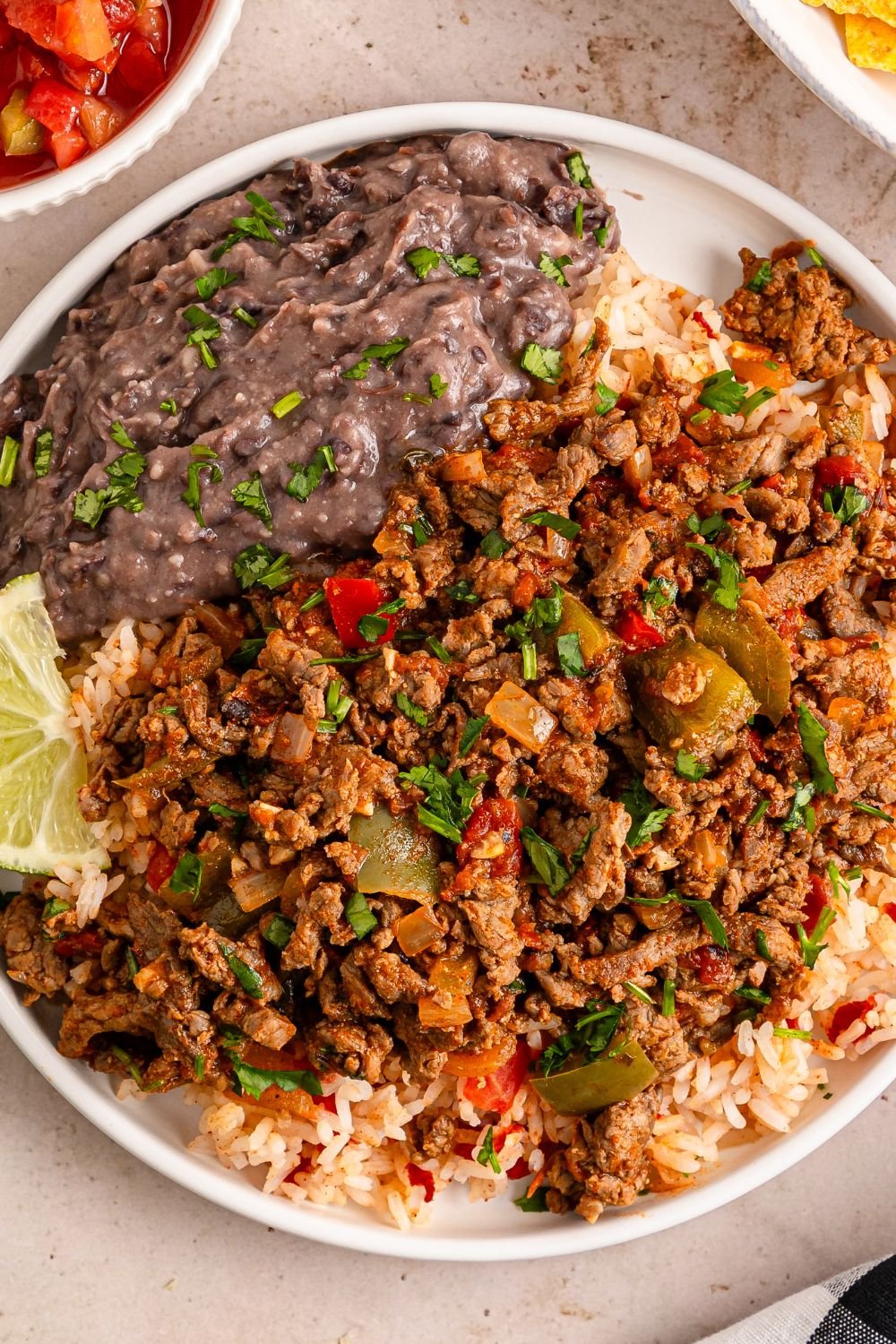 Carne Picada on a plate with rice, and black beans and other ingredients to showcase the meal 