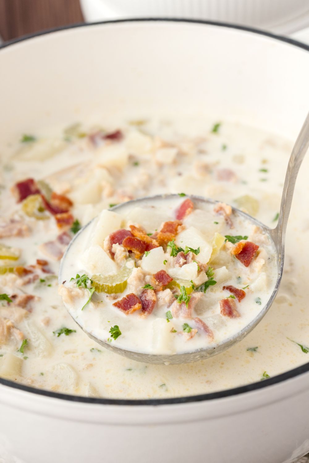 ladle of clam soup above the pot sitting on the table