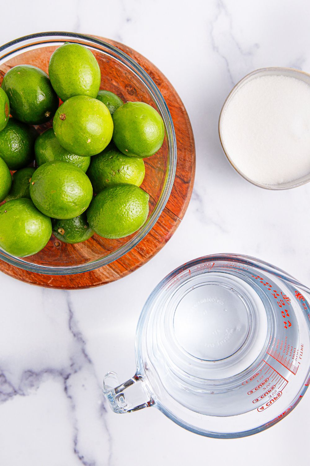 bowl of limes, water in a measuring cup, and bowl of sugar