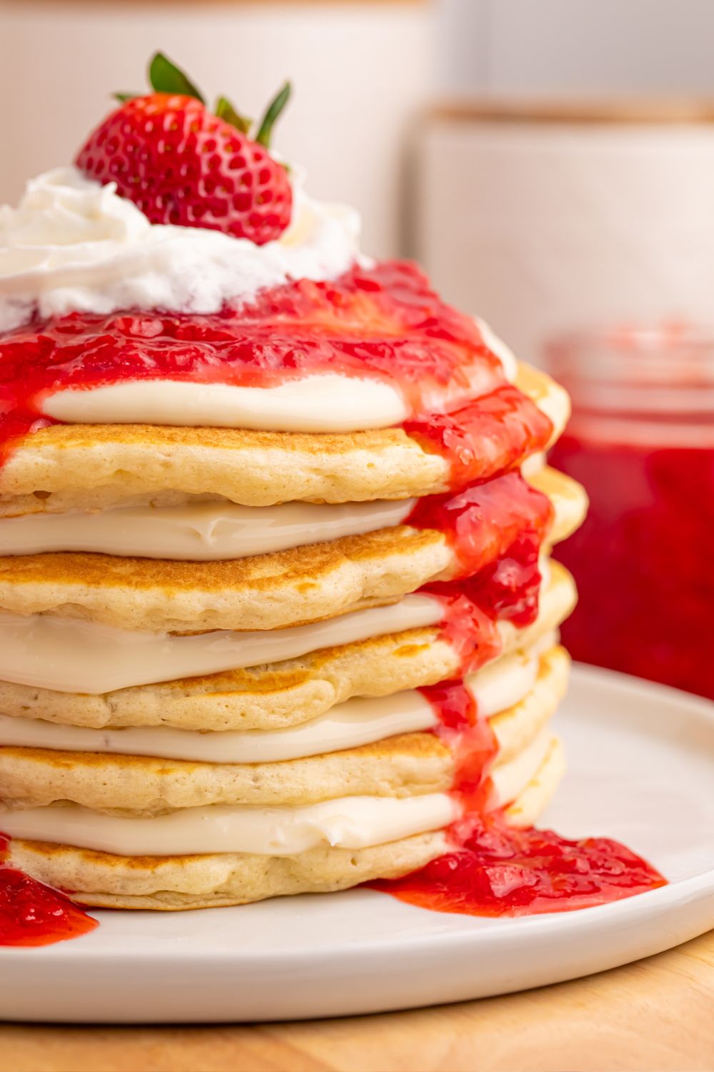 side view of pancakes with cream cheese spread on plate and strawberries on top for the Strawberry Cheesecake Pancakes