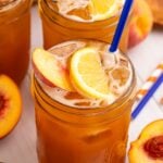 Peach Sweet Tea in mason jars sitting on table and garnished with a lemon wedge, peach slice, and a blue straw