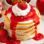 Strawberry Cheesecake Pancakes stacked on a plate with whipped cream a whole berry on top