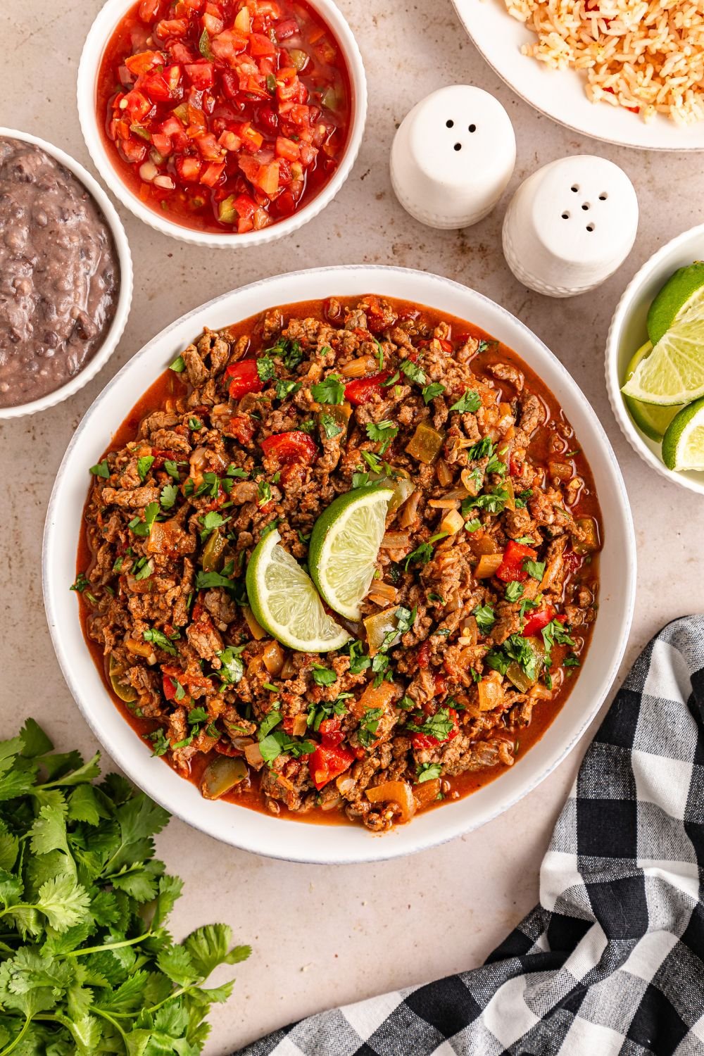 overhead bowl of carne picada with lime wedges on top and ingredients around the bowl