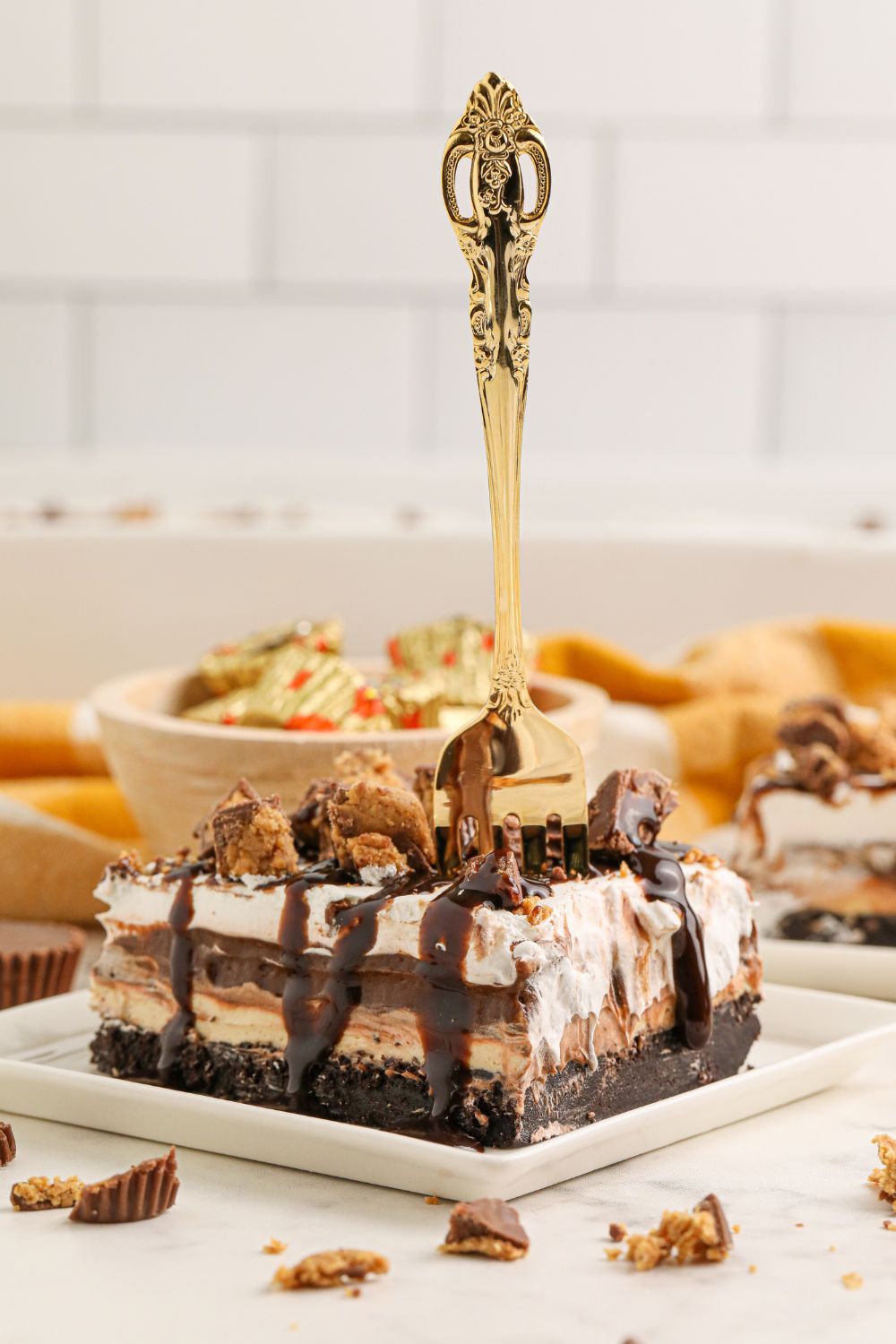 Reeses Lasagna slice on table with a fork in it  and a bowl of Reese's behind  it 