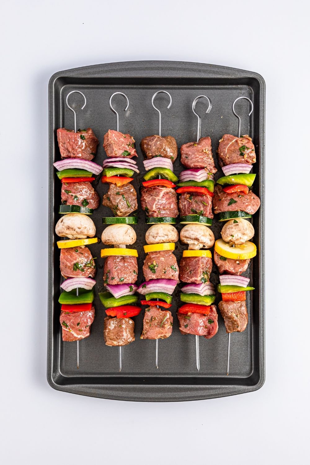 raw Marinated Beef Kabobs on a cookie sheet sitting on table 