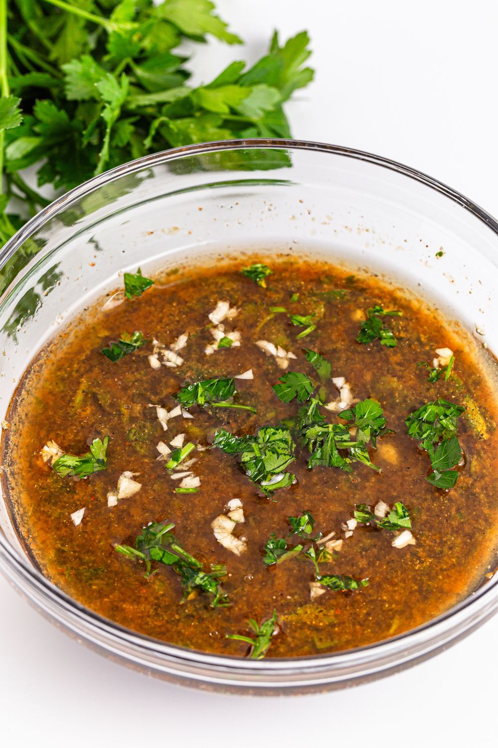 liquid marinade for Marinated Beef Kabobs in a bowl sitting on table with parsley behind it