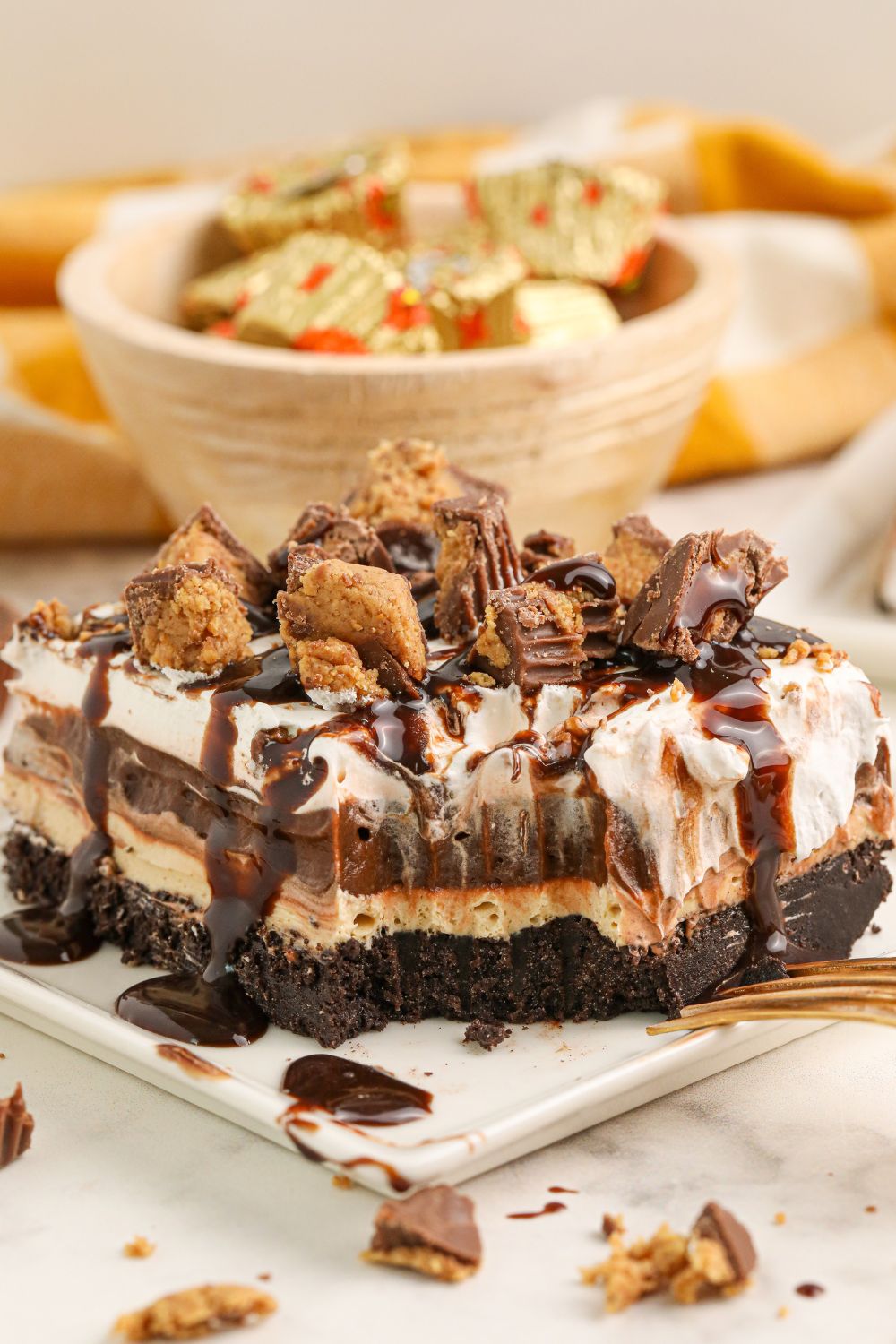 Reeses Lasagna on a plate with a bite taken out and a bowl of mini reese's in the background with wrappers on them