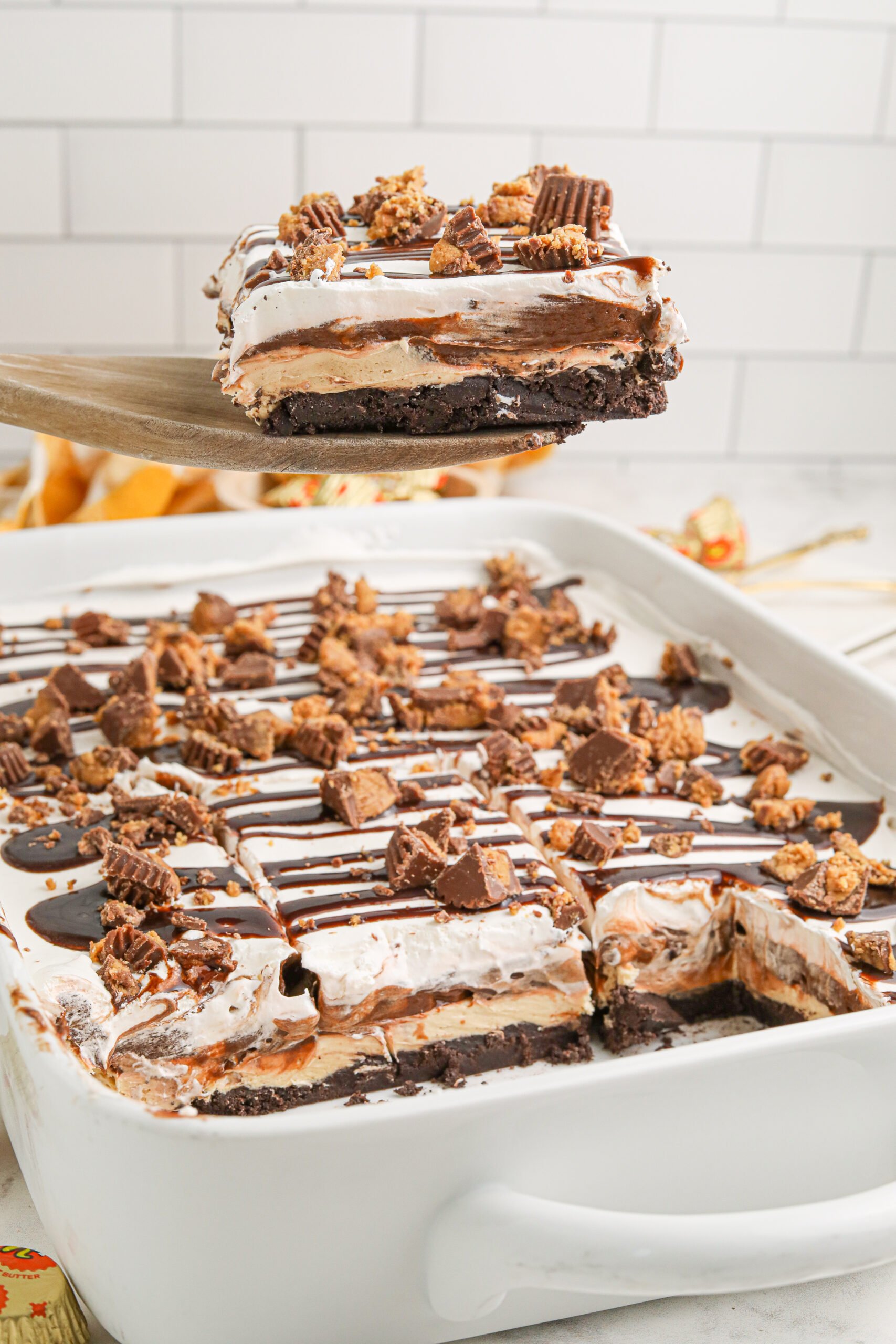 Reeses lasagna in a white baking pan with a piece being lifted up 