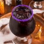 Witches Brew Cocktail sitting on a wooden cutting board with Halloween decor around it on table